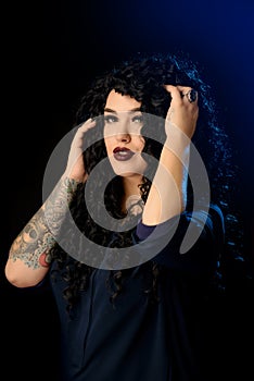 Portrait of a beautiful brunette girl with a tattoo in a dark dress against a black background with blue highlighters