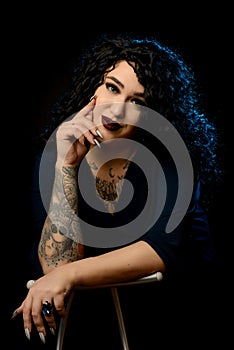 Portrait of a beautiful brunette girl with a tattoo in a dark dress against a black background with blue highlighters