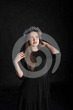 Portrait of beautiful brunette girl in wreath of dried flowers on black background, emotional concept