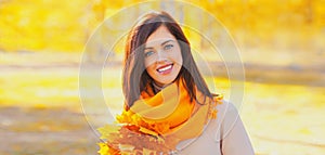Portrait of beautiful brunette smiling woman wearing scarf with yellow maple leaves in autumn park