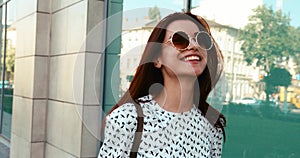 Portrait of the beautiful brunette in stylish cloth and sunglasses walking along the street and smiling at camera.