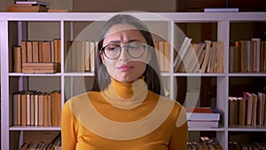 Portrait of beautiful brunette teacher in glasses turns head into camera to show disagreement and refusal at the library
