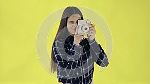 Portrait of Beautiful Brunette is Using Retro Camera on yellow Background in Studio. Young Woman Taking Photo.