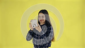 Portrait of Beautiful Brunette is Using Retro Camera on yellow Background in Studio. Young Woman Taking Photo.