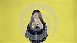 Portrait of Beautiful Brunette is Using Retro Camera on yellow Background in Studio. Young Woman Taking Photo.