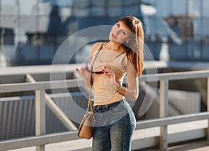 Portrait of beautiful brunette young woman in nice beige shirt, denim jeans and sunglasses. Genuine leather bag, high heels shoes