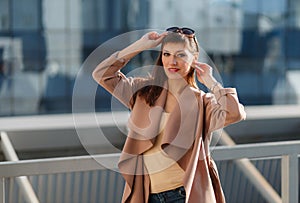 Portrait of beautiful brunette young woman in nice brown beige coat, denim jeans and sunglasses. Genuine leather bag, high heels