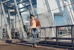 Portrait of beautiful brunette young woman in nice red brown jacket, denim jeans and sunglasses. Genuine leather bag, high heels