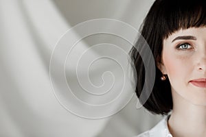 portrait of beautiful brunette young woman with short hair is looking at the camera against the background of a wall