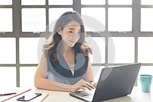 Portrait of beautiful business Asian woman sitting at her desk working on laptop computer in modern office. Smiling Successful
