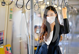 Portrait of beautiful business woman with hygiene mask stand with hold handrail in sky train along the way for working during