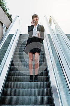 Portrait of beautiful business woman using smartphone in escalator on her way to work