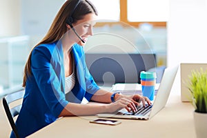 Portrait of beautiful business woman working at her desk with headset and laptop.