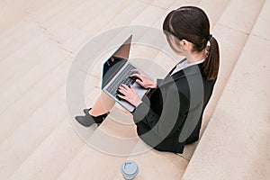 Portrait of beautiful businesswoman using laptop sitting on stairs in city street.