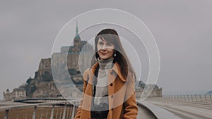 Portrait of beautiful calm brunette photographer woman smiling at camera at amazing Mont Saint Michel castle slow motion