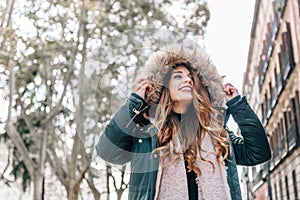 Portrait of beautiful caucasian blonde girl with coat, scarf and a big hood on a city street