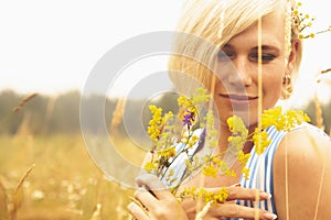 Portrait of beautiful caucasian blonde woman holding bouquet of flowers while walking outdoor through wild field in summer. Copy