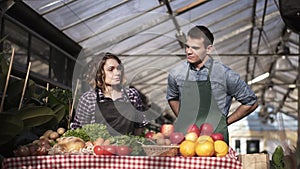 Portrait of beautiful caucasian farmers - man and woman putting aprons and gloves - selling organic food in farm market