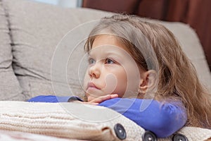 Portrait of beautiful caucasian little girl of 5 years lying on couch putting head on hands and looking aside very