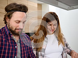 Portrait of a beautiful Caucasian pregnant woman smiling while cooking at home kitchen standing next to her husband