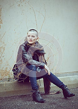 Portrait of beautiful Caucasian white young bald girl woman sitting on ground outside with shaved hair head in jacket