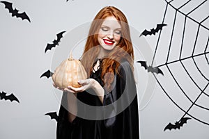 Portrait of beautiful caucasian witch holding pumpkin for celebrating Halloween.