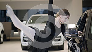 Portrait of beautiful caucasian woman dancing ballet in car dealership. Performance of slim ballerina in auto showroom