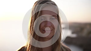 Portrait of the beautiful caucasian woman with long fair hair looking straight in the camera seriously and then smiling