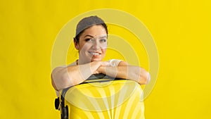 Portrait of a beautiful caucasian woman with a suitcase dreaming of vacation on a yellow background. A smiling girl