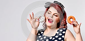 Portrait of beautiful cheerful fat plus size woman pin-up wearing a polka-dot dress isolated over light background, eating a donut