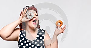 Portrait of beautiful cheerful fat plus size woman pin-up wearing a polka-dot dress isolated over light background, eating a donut