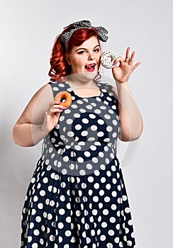 Portrait of beautiful cheerful fat plus size woman pin-up wearing a polka-dot dress isolated over light background, eating a donut