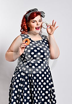 Portrait of beautiful cheerful fat plus size woman pin-up wearing a polka-dot dress  over light background, eating a donut