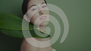 portrait of a beautiful cheerful girl stands in the studio with a green leaf palm plant on the background in the studio.