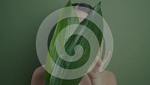 portrait of a beautiful cheerful girl stands in the studio with a green leaf palm plant on the background in the studio.