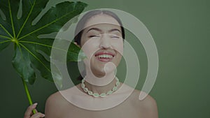 portrait of a beautiful cheerful girl stands in the studio with a green leaf palm plant on the background in the studio.