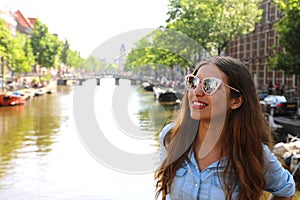 Portrait of beautiful cheerful girl with sunglasses looking to the side upon typical Amsterdam channel, Netherlands, Europe