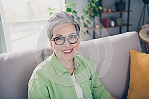 Portrait of beautiful cheerful mature age businesswoman wearing green shirt sitting on divan enjoying home comfort