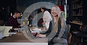 Portrait of beautiful cheerful young Caucasian blonde boss business woman posing with laptop at modern loft office.