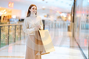 Portrait of beautiful cheerful young woman holding in hands shopping paper bags with purchase standing in mall