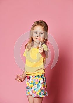 Portrait of a beautiful and confident girl child in summer clothes showing thumbs up isolated one pink