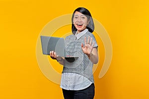 Portrait of beautiful confident young Asian woman holding laptop and pointing at number five with cheerful expression