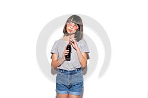 Portrait of beautiful crazy smiling brunette woman drinking soda from bottle with straw in casual summer clothes with no makeup