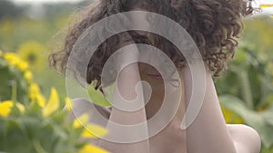 Portrait of a beautiful curly girl posing and looking at the camera touching her hair standing on the sunflower field