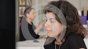 Portrait of beautiful curly-haired woman with piercing that looks at monitor.