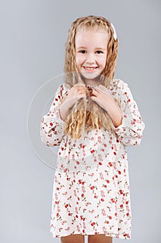 Portrait of a beautiful curly little girl in an elegant floral dress stands, laugh and looks into the camera in the studio on a