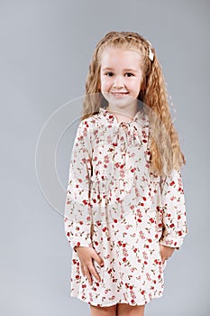 Portrait of a beautiful curly little girl in an elegant floral dress stands, laugh and looks into the camera in the studio on a