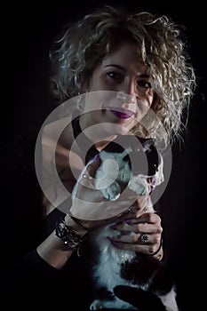 Portrait of a beautiful curly and smiling blonde woman holding a black and white cat