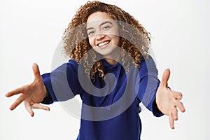 Portrait of beautiful curly woman reaching hands for hug, receiving smth in hands, smiling and cuddling, standing over