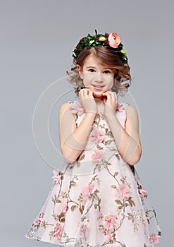 Portrait of a beautiful cut little girl in an elegant dress with a wreath of fresh flowers on her head stands, lauht and looks